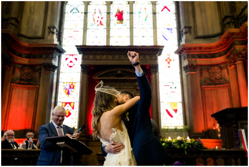 Bride and groom celebrate their first kiss in front of stained glass window