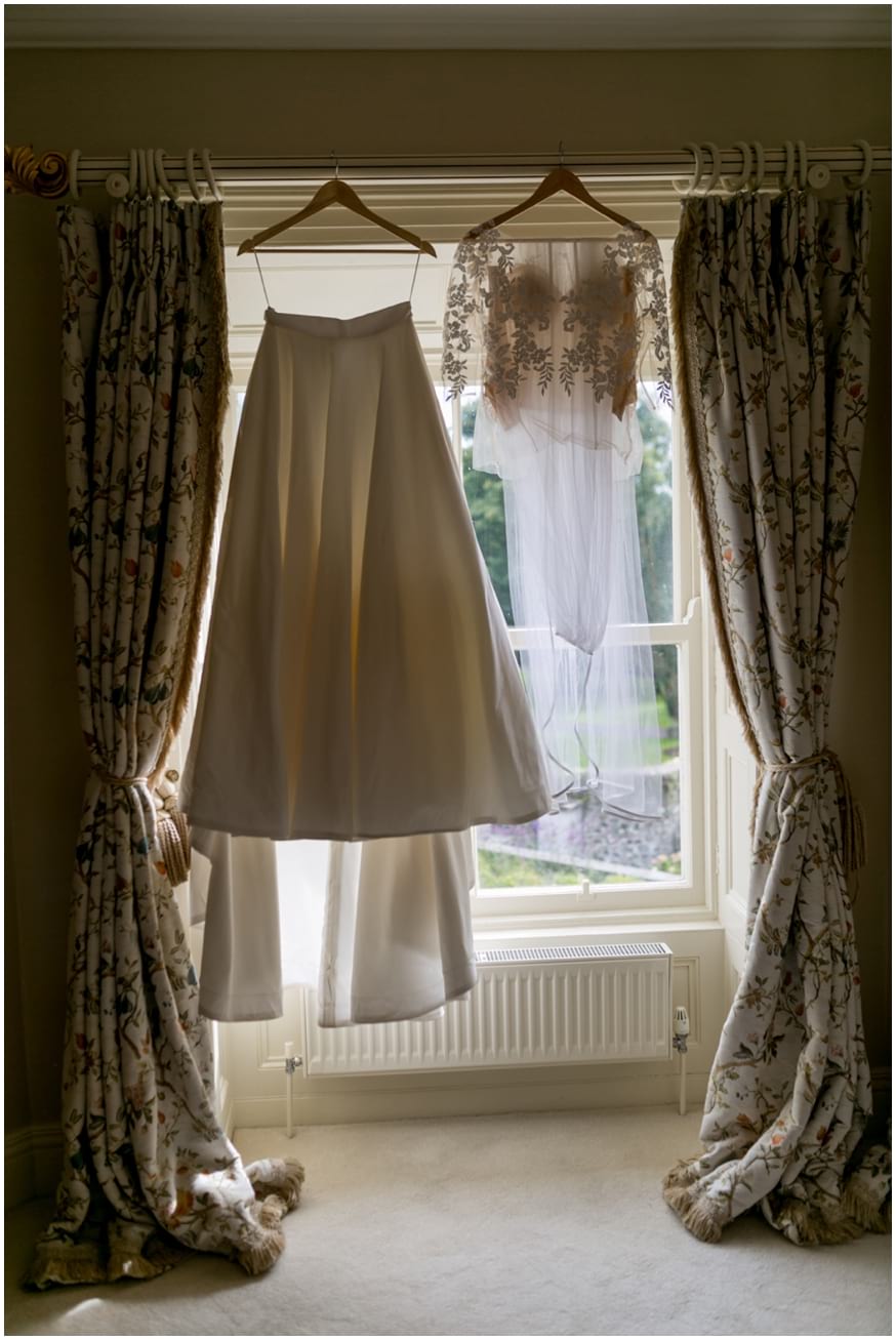 Beautiful delicate lace wedding dress hangs in the window of brides room 
