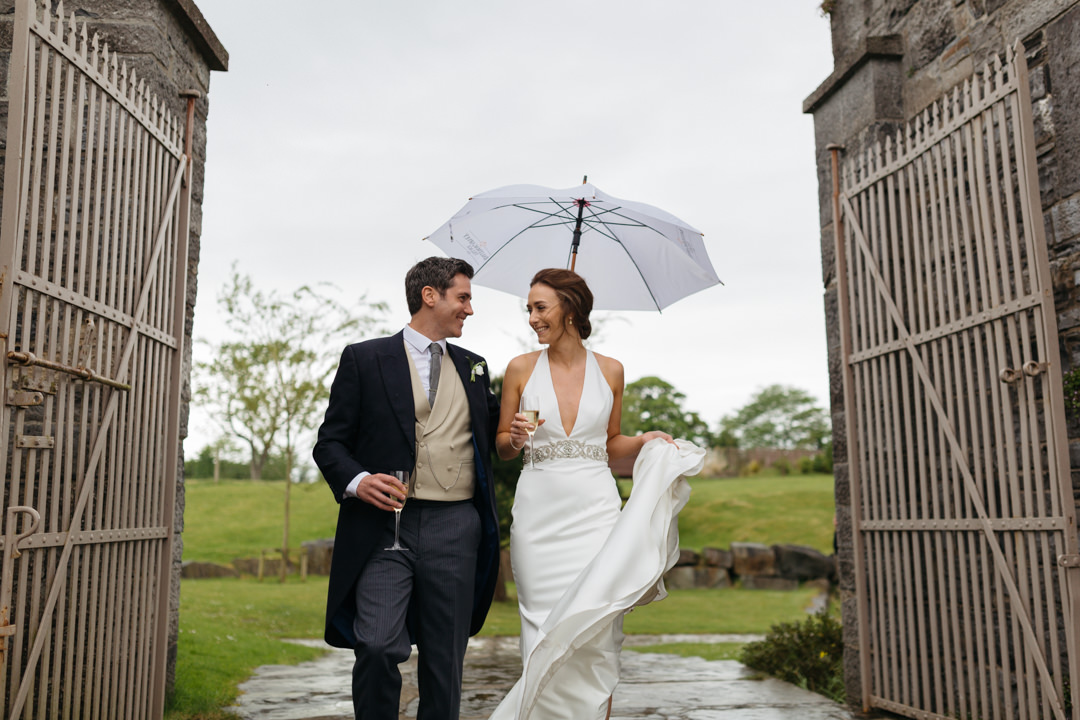 Bride and groom walk through a gate with an umbrella 