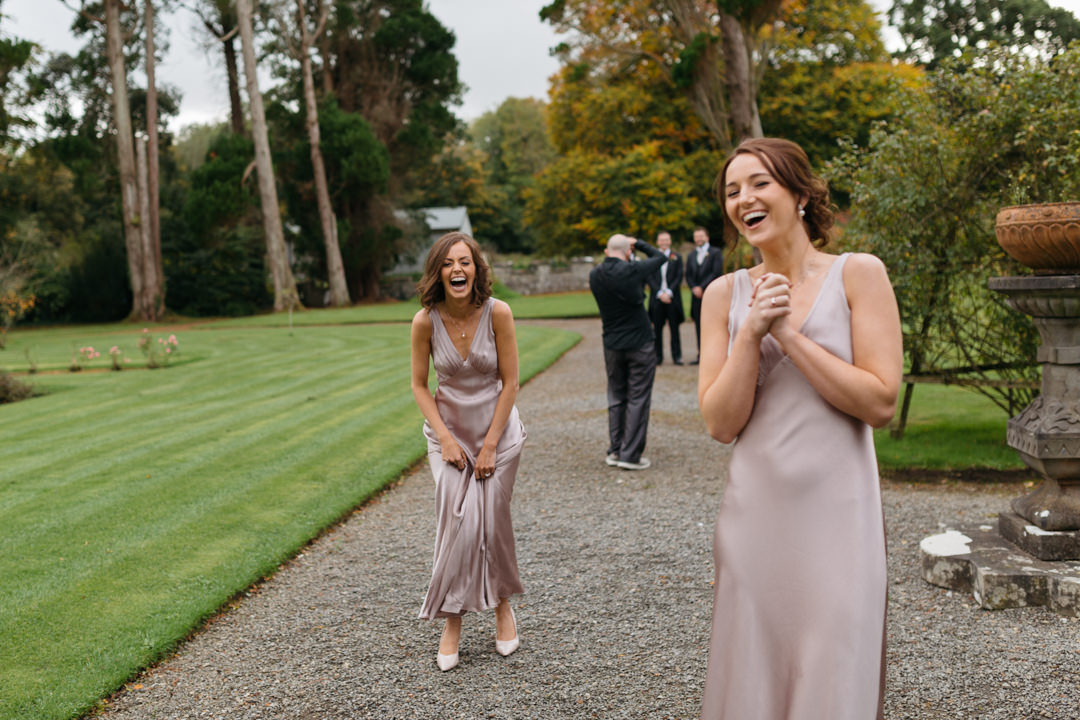Bridesmaids in blush pink silk dresses laugh in Markree Castle gardens 